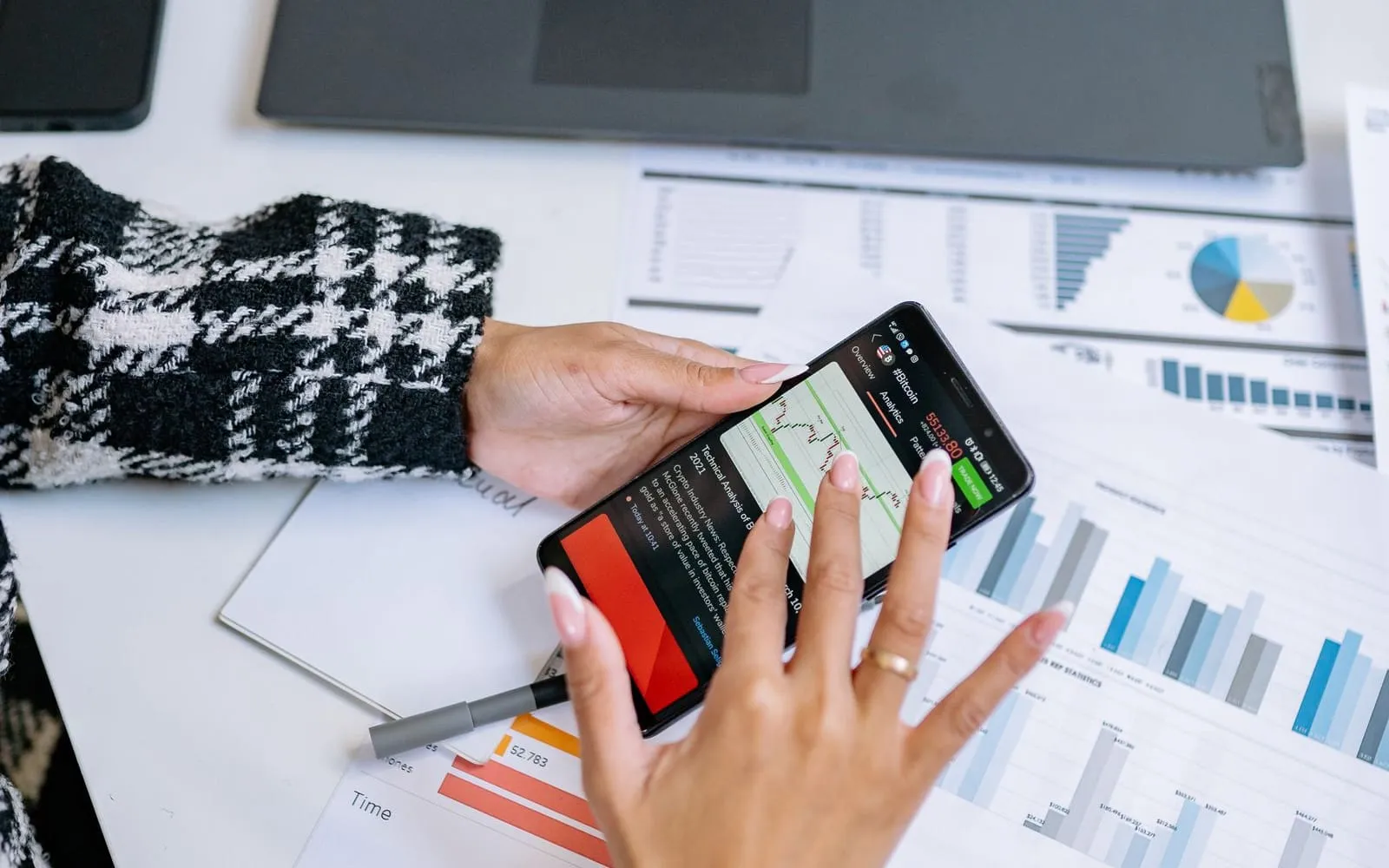 Mãos segurando o celular sobre gráficos impressos numa mesa