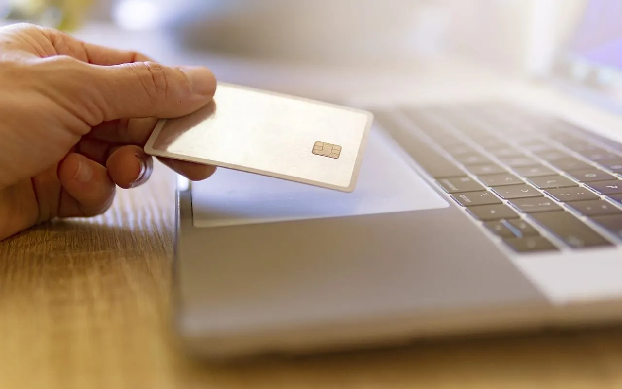 Mão segurando um cartão sem marca ao lado do teclado de um notebook