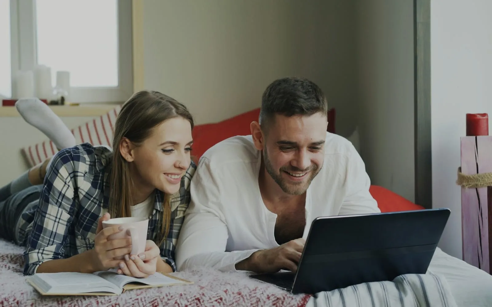 Casal deitado na cama olhando o notebook juntos e sorrindo