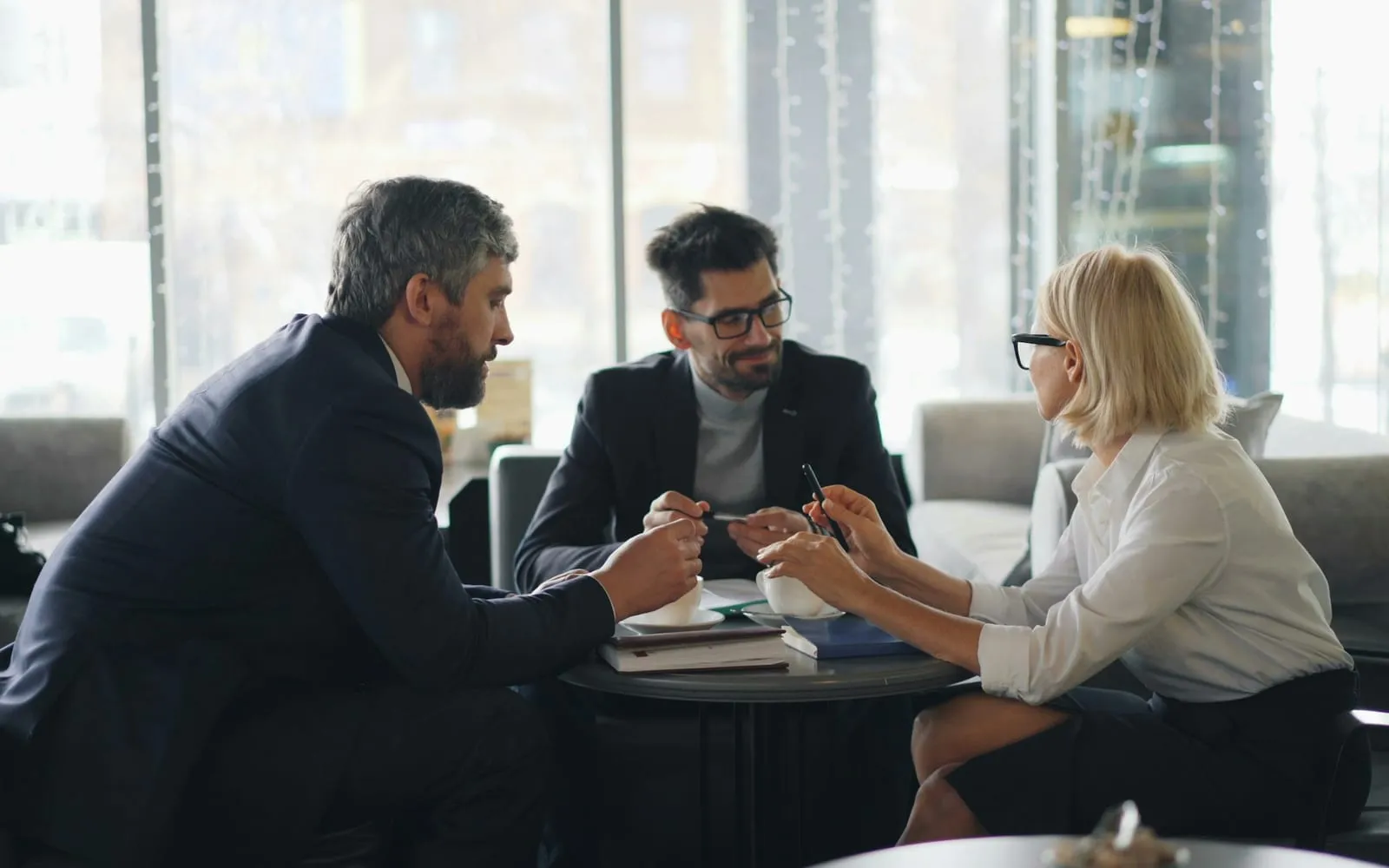 Três profissionais conversando sobre um projeto em volta de uma mesa, com cadernos e café