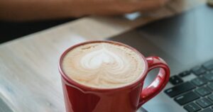 Pessoa em rotina de trabalho com laptop, smartphone e café, representando organização financeira no dia a dia